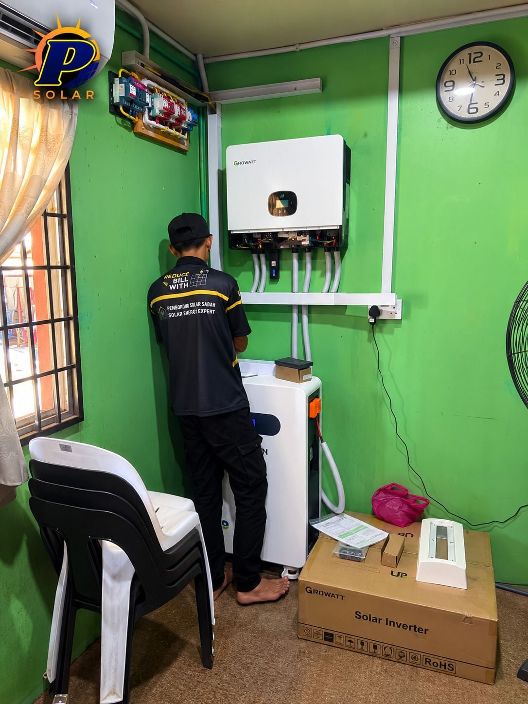 A technician in the company polo working at a wall-mounted Growatt inverter, with the battery cabinet below.