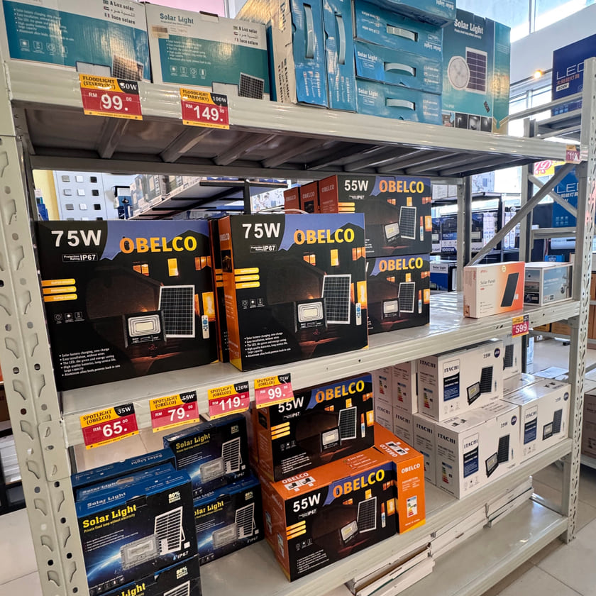 Retail shelving of boxed solar floodlights and spotlights above our printed shop price cards.
